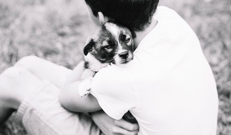 um menino sentado ao chão segurando no colo um cachorrinho.