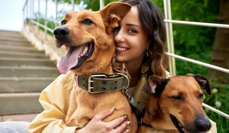 uma mulher abraçada com seus dois cachorros comemorando o dia mundial dos cachorros.