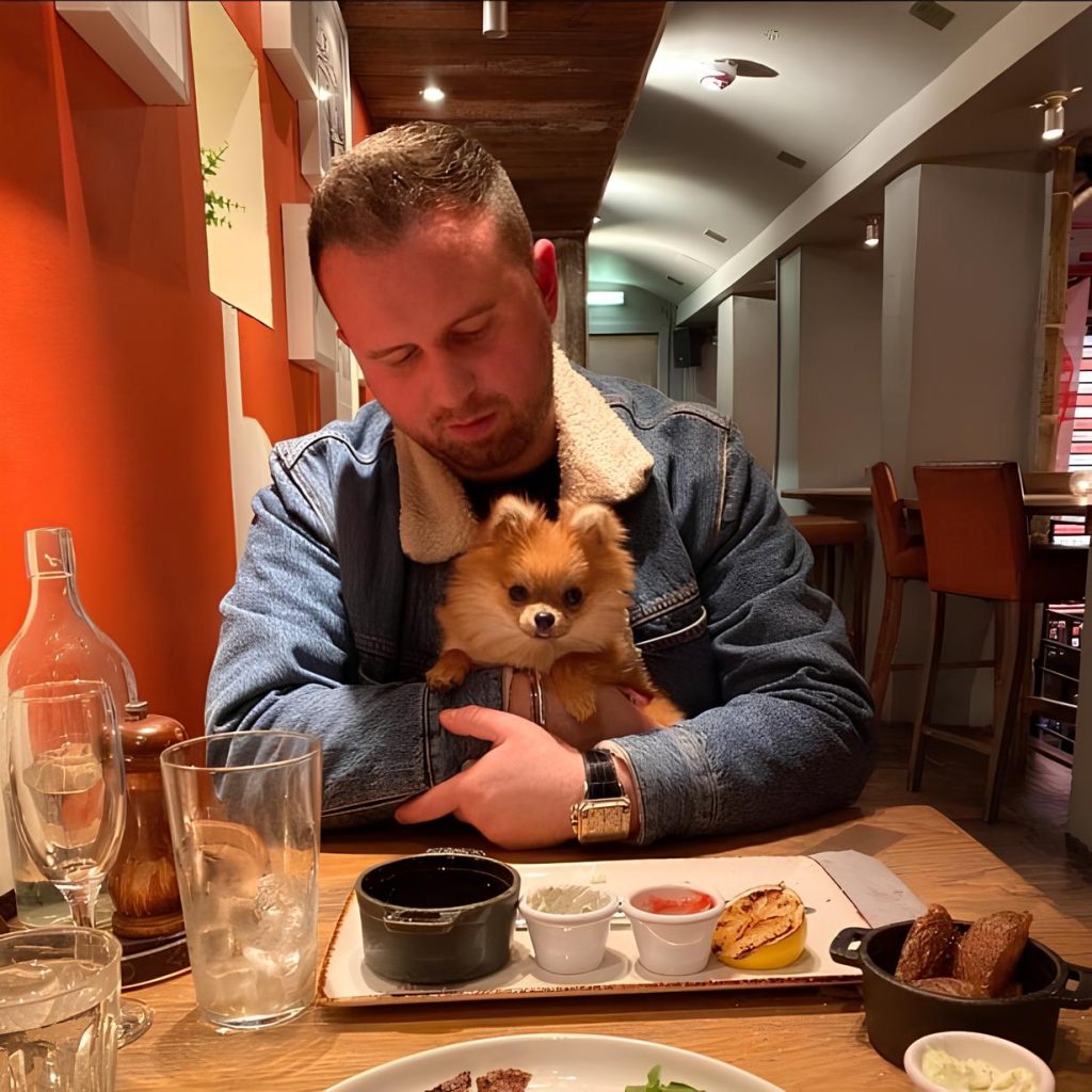 um homem em um restaurando segurando em seu colo um lulu da pomerânia.