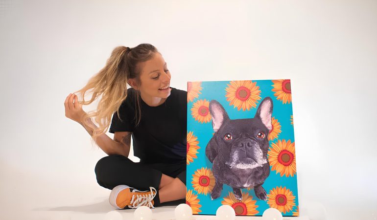 uma moça sentado ao chão segurando um quadro pintado de um cachorro.
