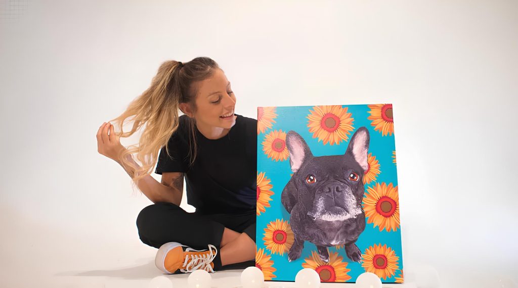uma moça sentada no chão segurando um quadro pintado de um cachorro.