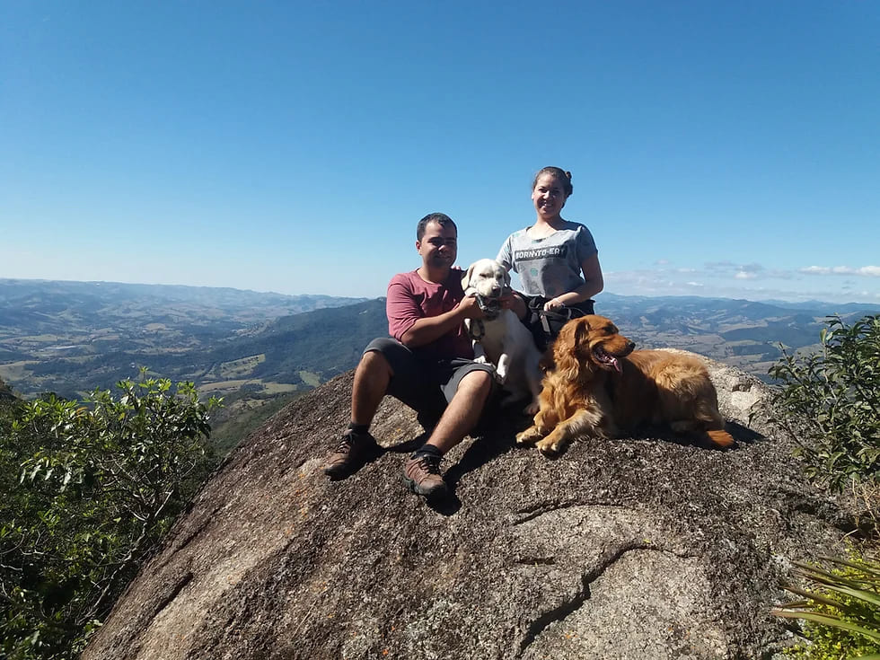 um casal com dois cachorro em cima de uma pedra no alto de montanhas fazendo Trilhas Pet-Friendly.