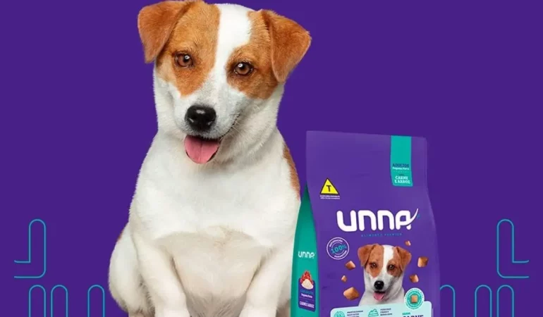 um cachorro sentado e ao seu lado um saco de ração da marca UNNA.